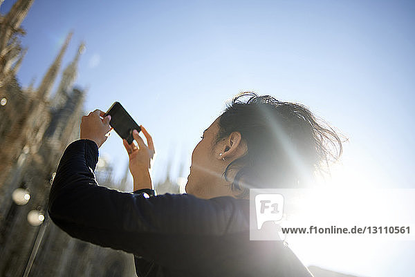 Low angle view of woman photographing while standing against clear sky