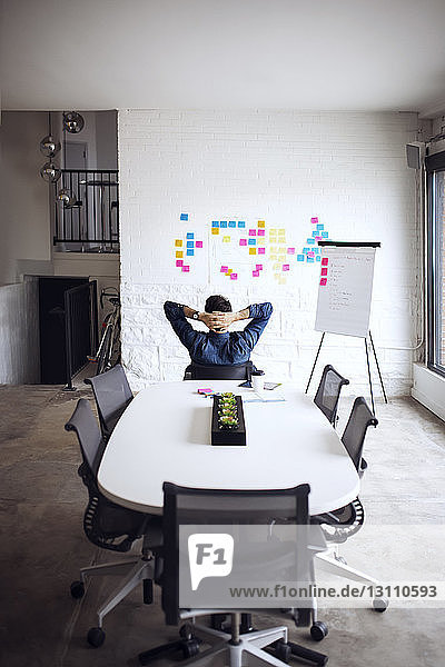Rückansicht eines Geschäftsmannes  der sich Haftnotizen ansieht  während er in einem kreativen Büro auf einem Stuhl sitzt