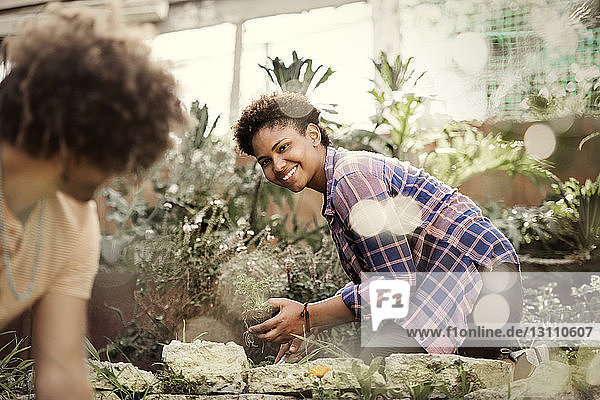 Happy woman looking at friend while gardening in community garden