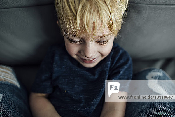 Hochwinkelaufnahme eines lächelnden Jungen  der zu Hause auf dem Sofa sitzt