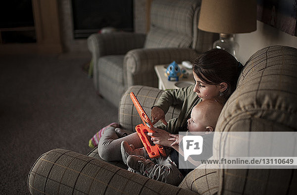 Mädchen hält Spielzeug in der Hand  während sie zu Hause mit ihrem Bruder auf einem Sessel spielt
