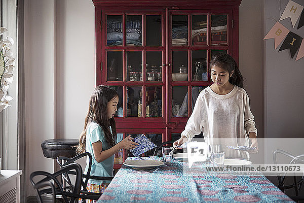 Sisters arranging dining table at home for surprise birthday celebration