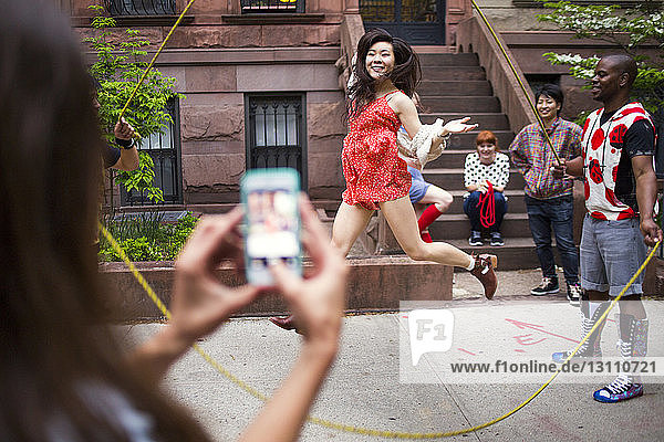 Frau fotografiert Freunde  die auf dem Bürgersteig Doppel-Holländisch spielen