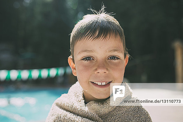 Porträt eines in ein Handtuch gewickelten glücklichen Jungen am Poolufer stehend