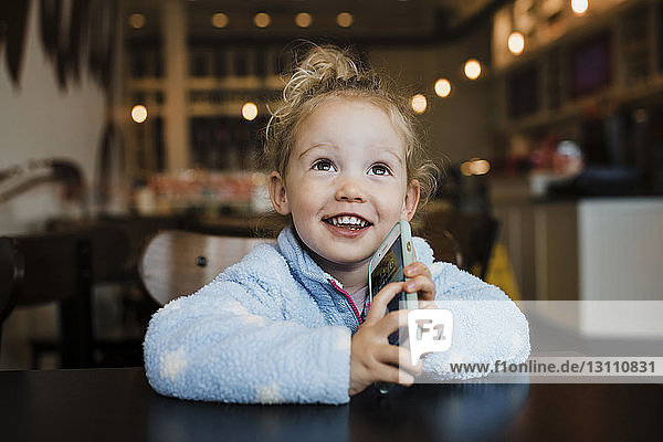Close-up of smiling girl holding smart phone while sitting at table in restaurant