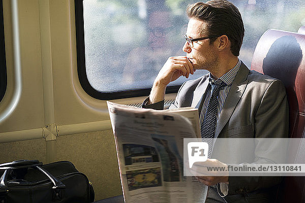 Nachdenklicher Geschäftsmann hält Zeitung in der Hand  während er im Zug reist