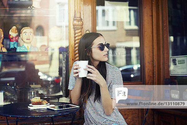 Schöne Frau hält Kaffee in der Hand und sitzt im Straßencafé