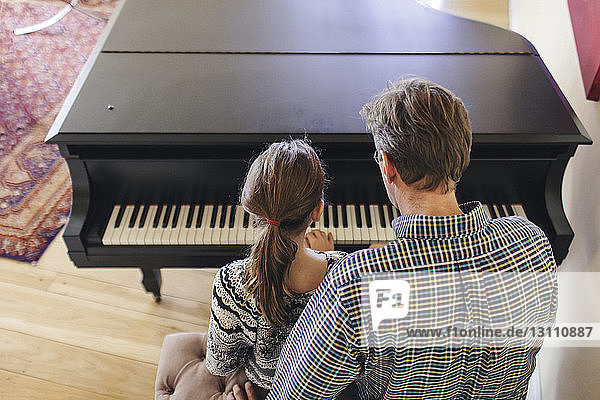 Rear view of father assisting daughter in playing piano while sitting at home