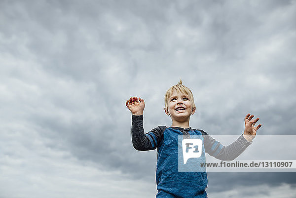 Low angle view of cheerful boy standing against cloudy sky