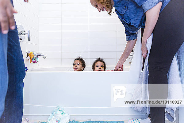 Happy mother looking at cute daughters sitting in bathtub