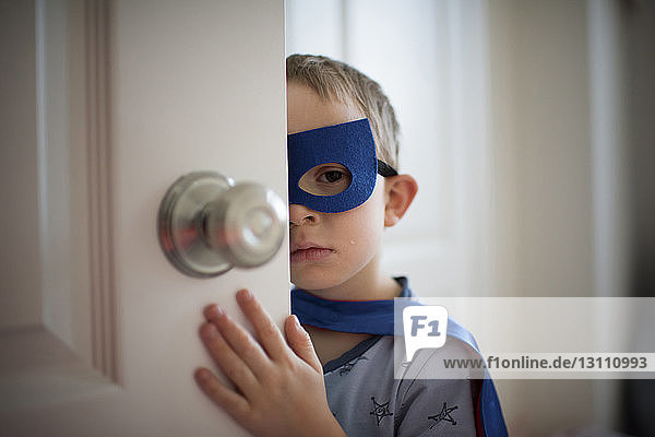 Nahaufnahme eines Jungen im Superhelden-Kostüm  der wegschaut  während er zu Hause an der Tür steht
