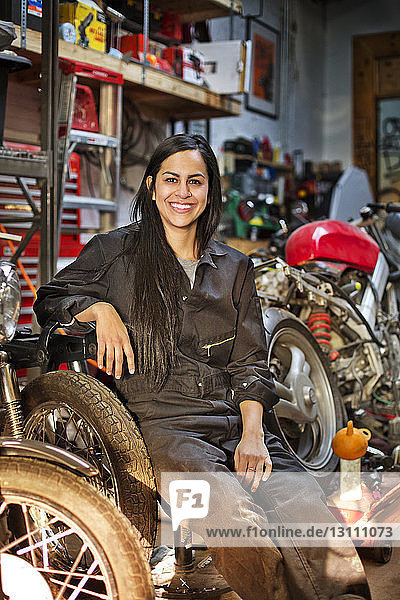 Porträt einer glücklichen Mechanikerin  die in der Werkstatt sitzt