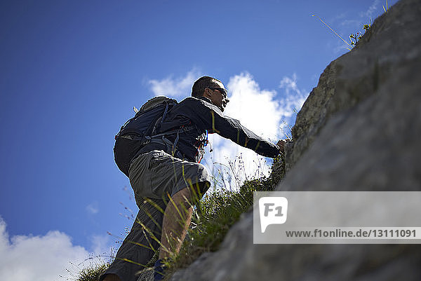 Low angle view of hiker climbing mountain against sky during sunny day