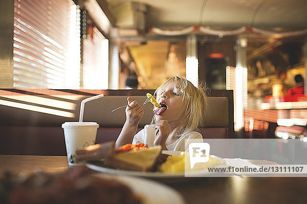 Girl eating food while sitting at restaurant