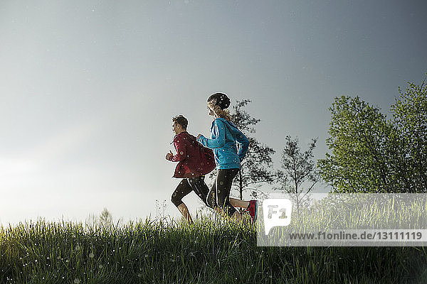Side view of determined athletes running on grassy field during sunset