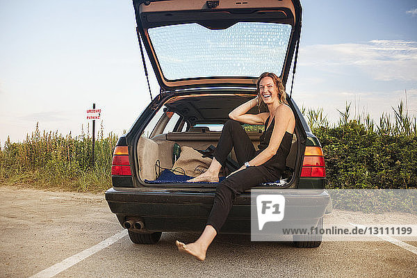 Glückliche Frau sitzt im offenen Kofferraum eines Autos auf der Straße