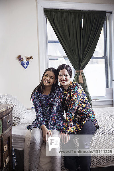 Portrait of mother and daughter sitting on bed at home