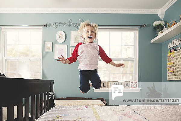 Cute girl jumping on bed against wall at home