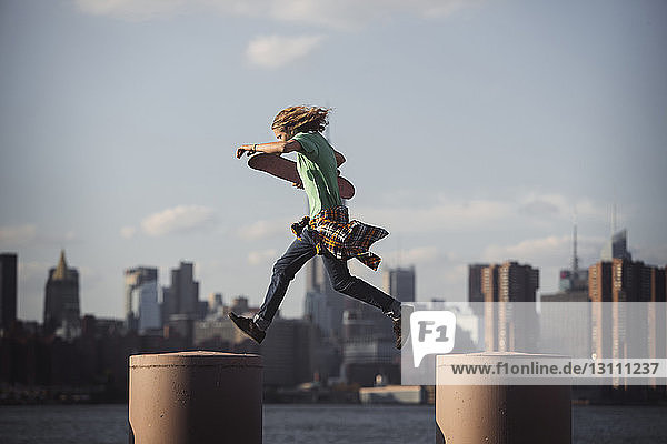 Mann hält Skateboard  während er in der Stadt auf Säulen springt