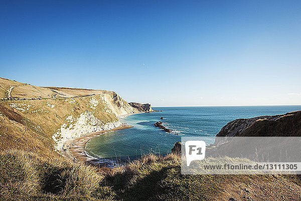 Scenic view of sea and cliffs against clear blue sky