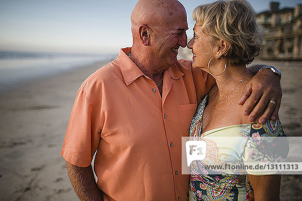 Smiling senior couple looking at each other while standing by sea against sky