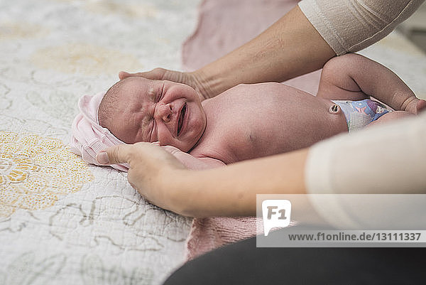 Cropped hands of mother holding crying newborn daughter on bed