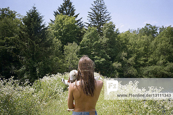 Rear view of topless woman holding goat with trees in background