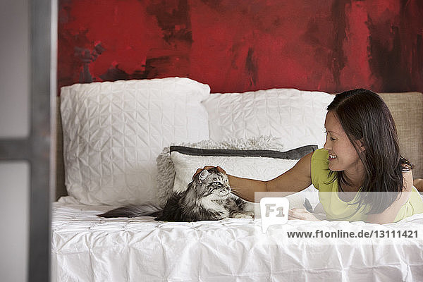 Happy woman lying with cat on bed at home