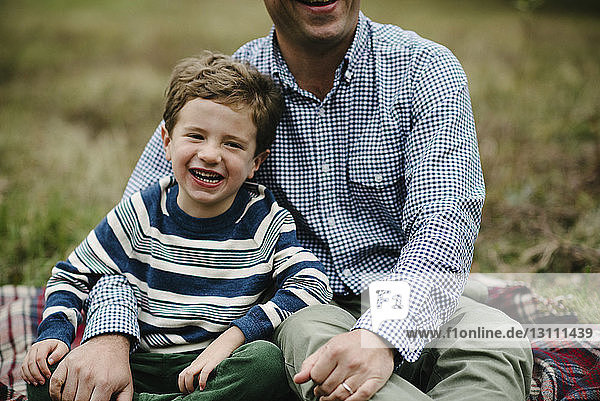 Midsection of father with son sitting on blanket at park