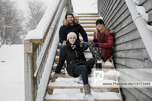 Porträt von lächelnden Freunden  die auf schneebedeckten Stufen sitzen