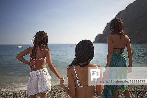 Mother and daughters holding hands while looking at sea against sky