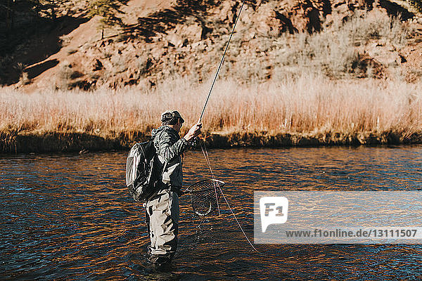 Side view of hiker with backpack fishing in river at forest