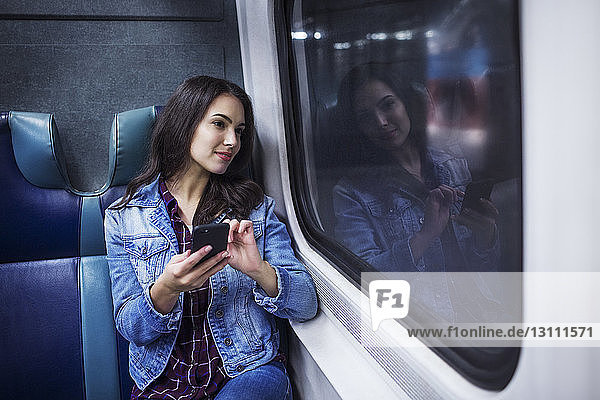 Nachdenkliche Frau mit Handy  die während einer Zugfahrt wegschaut