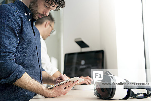 Ingenieur  der einen Tablet-Computer benutzt  während ein Kollege den Computer im Büro benutzt