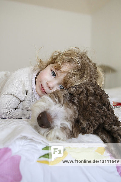 Portrait of happy girl relaxing with dog on bed at home