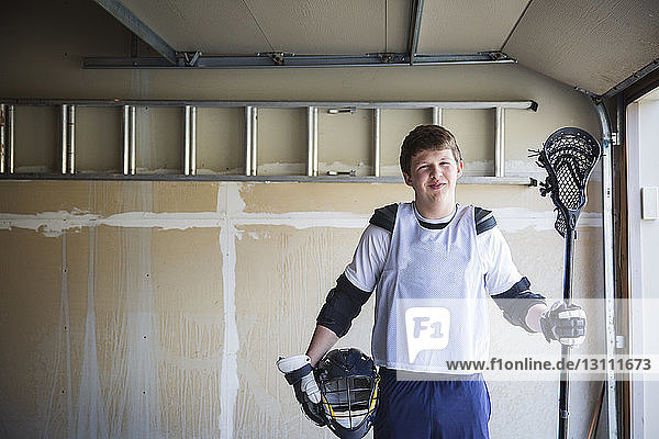Portrait of smiling man holding helmet and lacrosse stick at home