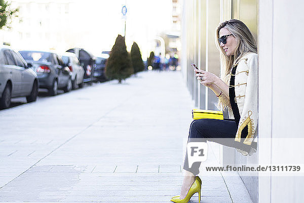 Woman using mobile phone while sitting on window sill