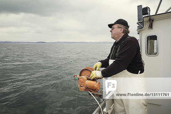 Side view of fisherman standing on fishing boat against cloudy sky
