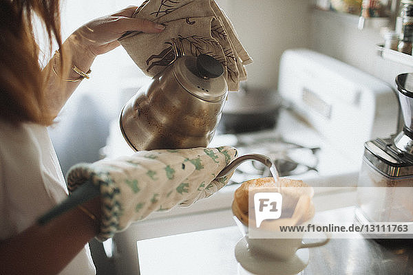 Ausgeschnittenes Bild einer Frau  die zu Hause Tee in die Tasse gießt