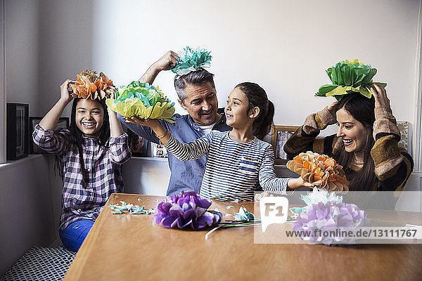 Fröhliche Familie spielt mit selbstgemachten Papierblumen  während sie am Tisch sitzt