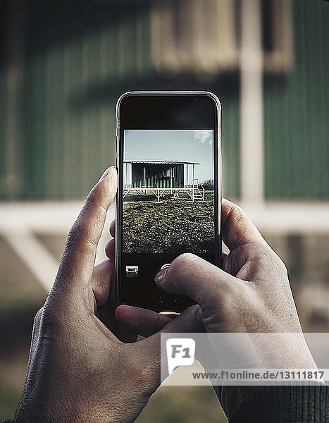 Cropped hands of man photographing house with mobile phone