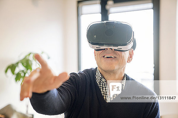 Lächelnder Mann zeigt auf ihn  während er zu Hause einen Virtual-Reality-Simulator trägt