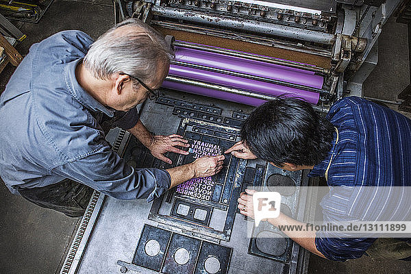 Schrägansicht von Arbeitern  die in der Werkstatt den Buchdruck an Maschinen reparieren