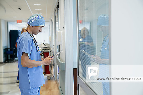 Chirurg benutzt Tablet-Computer  während er im Krankenhauskorridor steht