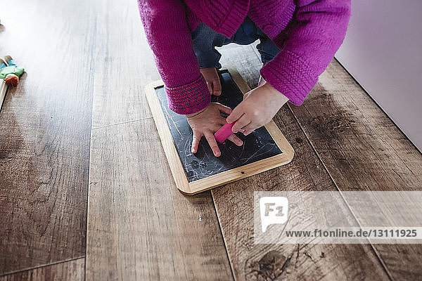 Low section of girl crouching with slate and eraser on hardwood floor