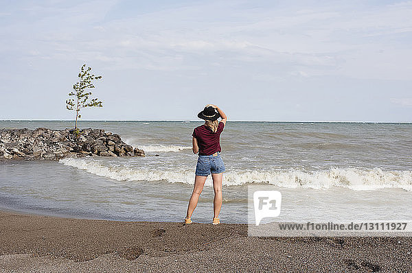 Rear view of woman wearing hat while standing at beach against sky