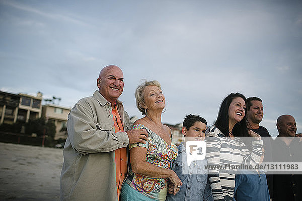 Happy family standing at beach against sky during sunset