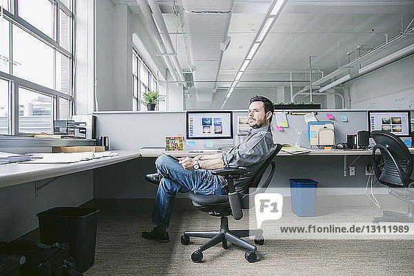Seitenansicht eines Geschäftsmannes mit Tablet-Computer  der beim Entspannen auf einem Stuhl wegschaut