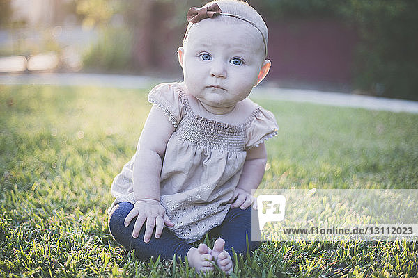 Portrait of cute baby girl sitting on grassy field at backyard