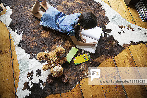 Hochwinkelaufnahme eines Mädchens  das auf einem Teppich liegt und zu Hause studiert